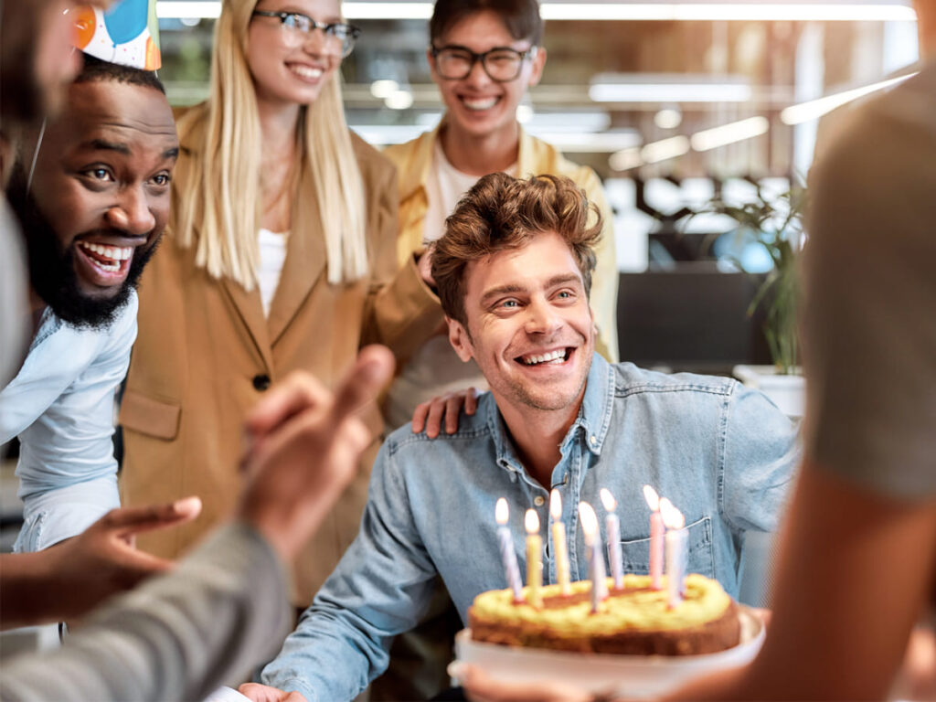 eine Gruppe von Freunden stehen um einen Mann der Geburtstag hat und eine Torte in der Hand hat